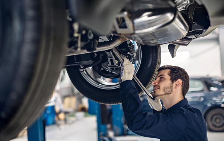 profissional homem com roupa azul apertando parafuso de carro suspenso demonstrando como fazer alinhamento e balanceamento de carro
