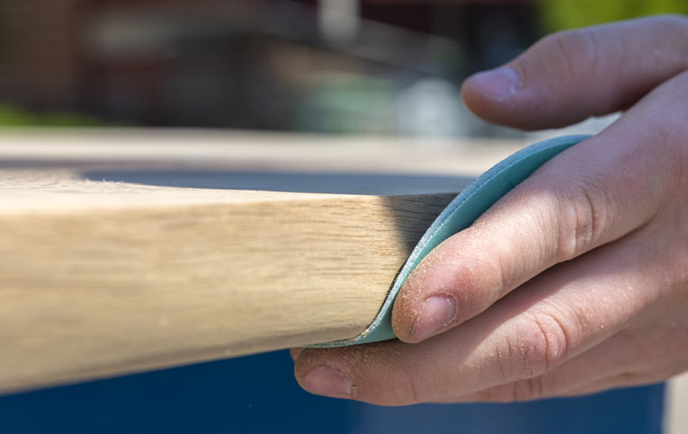 mão segurando um dos tipos de lixa para madeira em lateral de superficie clara