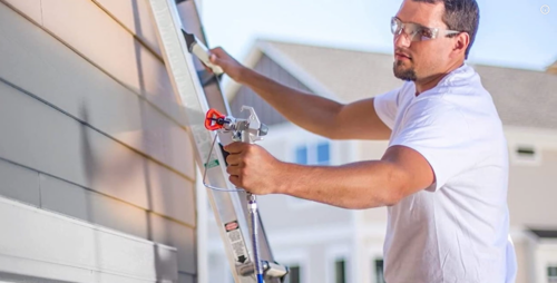 Pessoa utilizando uma pistola de pintura Airless para pintar a lateral de uma casa.